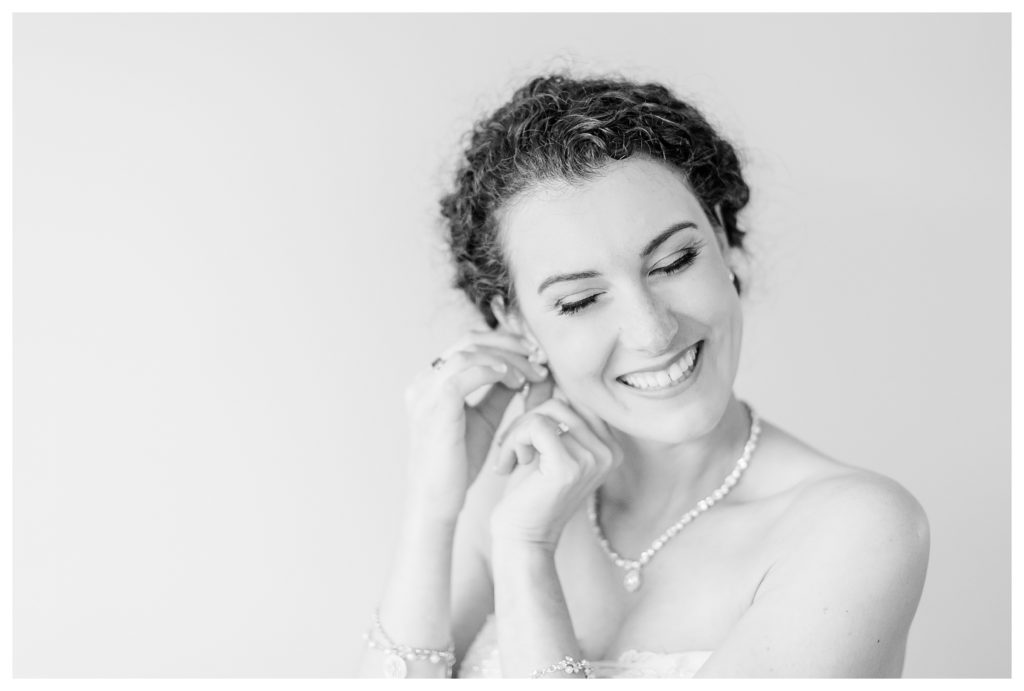 Bride laughing while putting on her earrings.